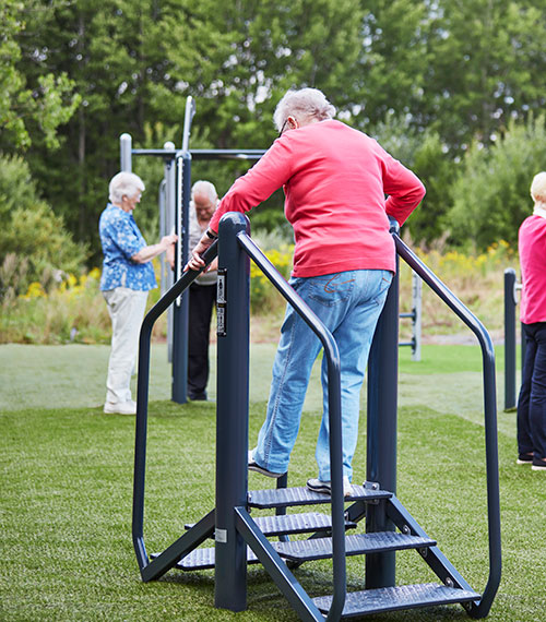 Elderly woman is exercising on an outdoor stair equipment.